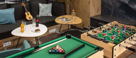 A pool table with billiard balls, a foosball table, a guitar, and a sofa with cushions.
