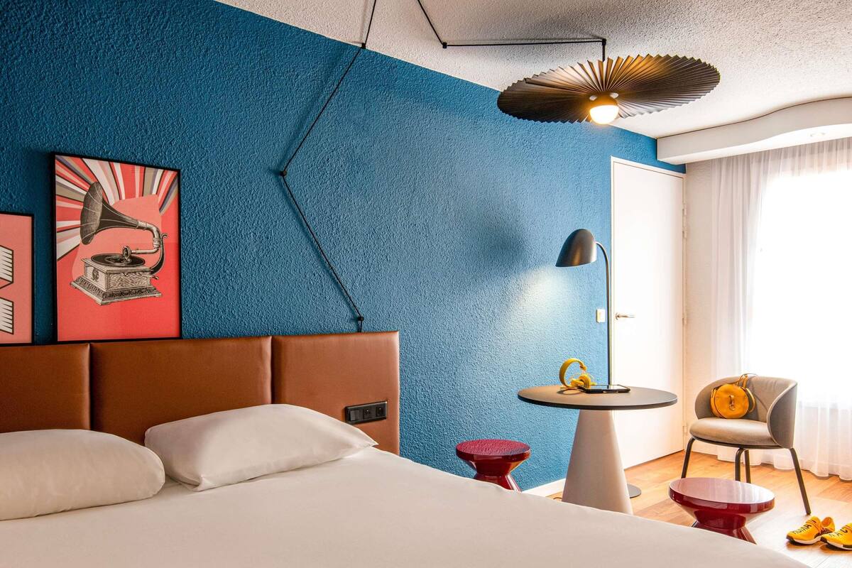 Quarto de hotel moderno com uma cama grande, uma pequena mesa redonda, uma cadeira e um lustre de teto exclusivo.