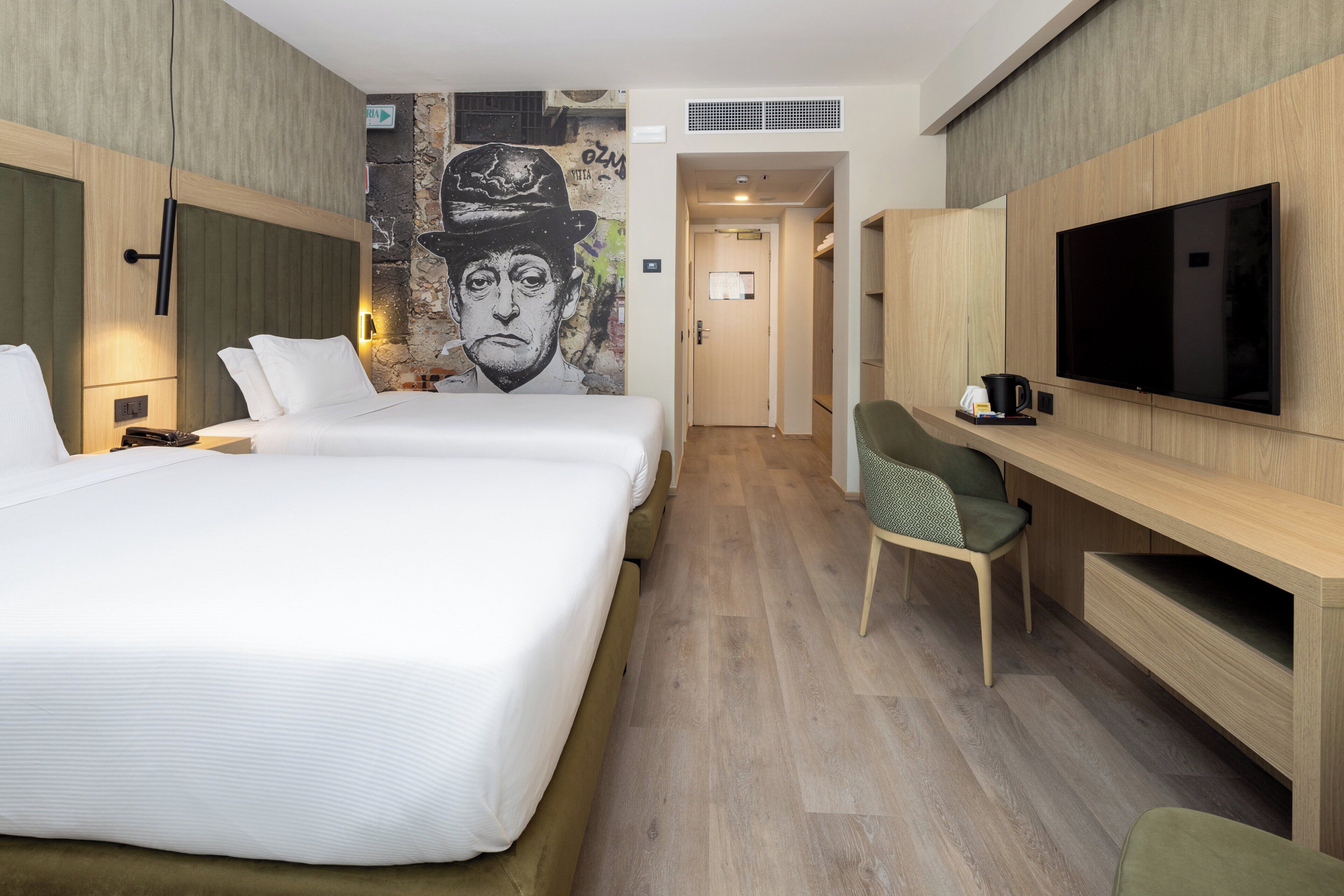 A hotel room with two beds, a television, a desk, and a mural on the wall.
