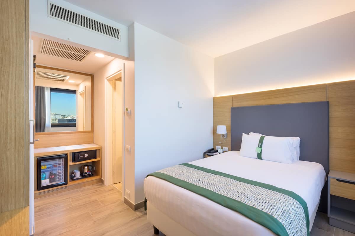 Une chambre d’hôtel avec un lit, une table de chevet et une vue sur la ville par la fenêtre.