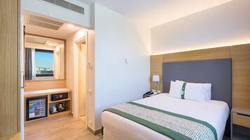 A hotel room with a bed, bedside table, and a view of the city through the window.