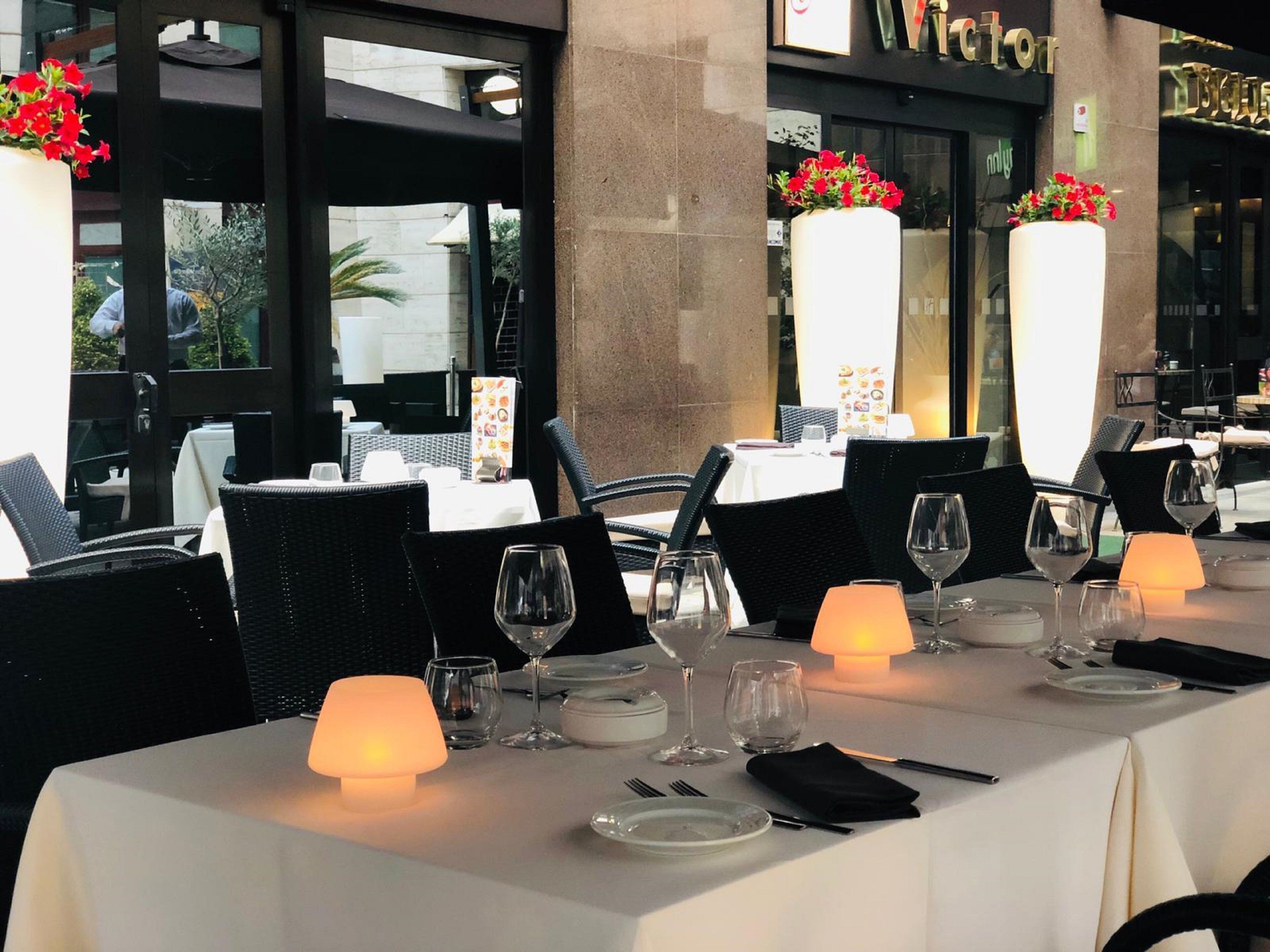 A restaurant with tables set for dining, featuring white tablecloths, black chairs, and candlelit lamps.