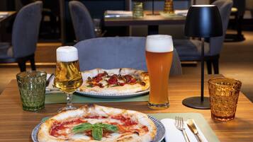 Une table à manger avec deux pizzas, deux verres de bière et une lampe.