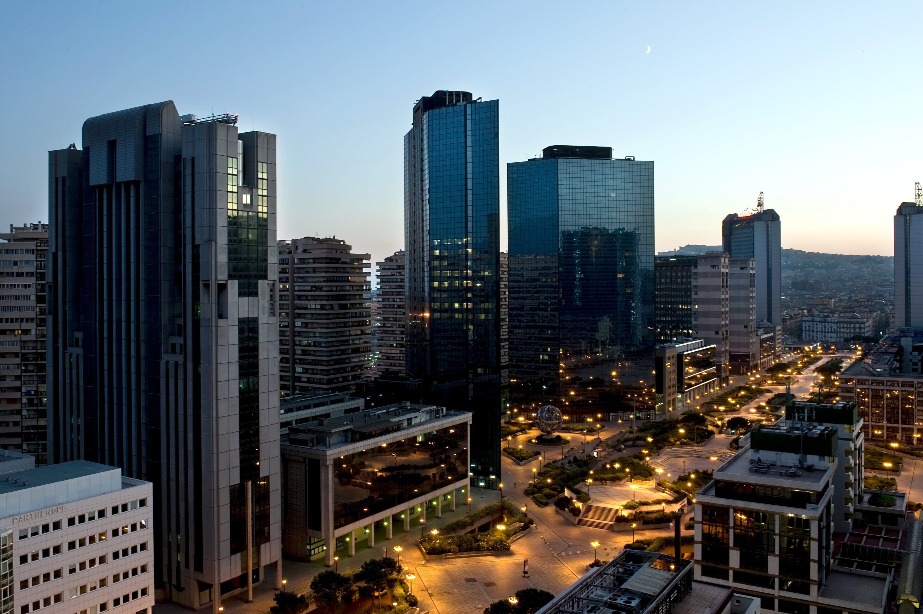 A cityscape with modern high-rise buildings, a central roundabout, and a well-lit urban area.