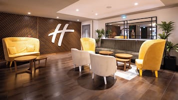 Een moderne lobby met een receptiebalie, zithoek en een decoratieve wand met een geometrisch patroon.