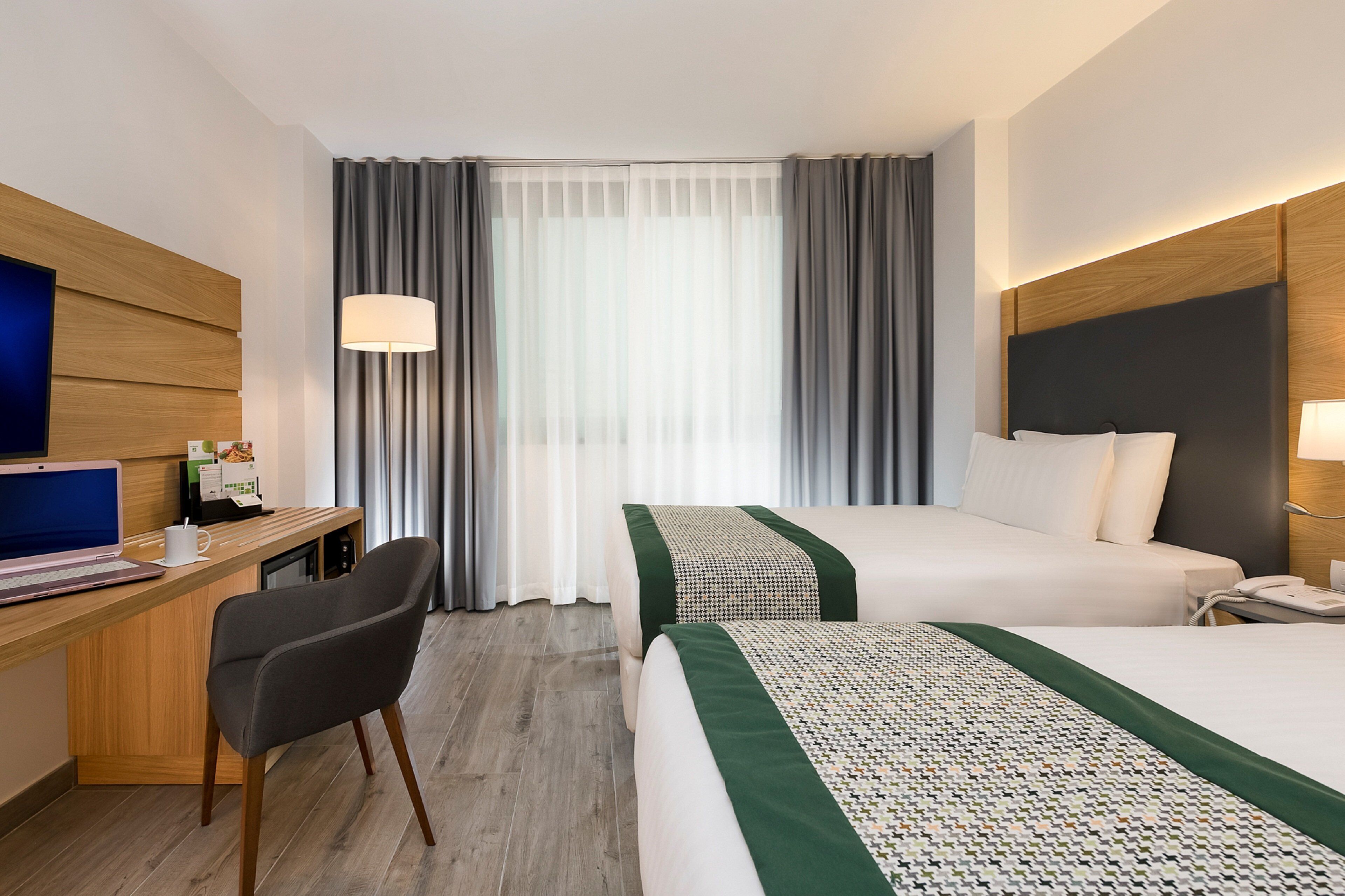 A hotel room with a desk, two beds, a chair, and a TV.