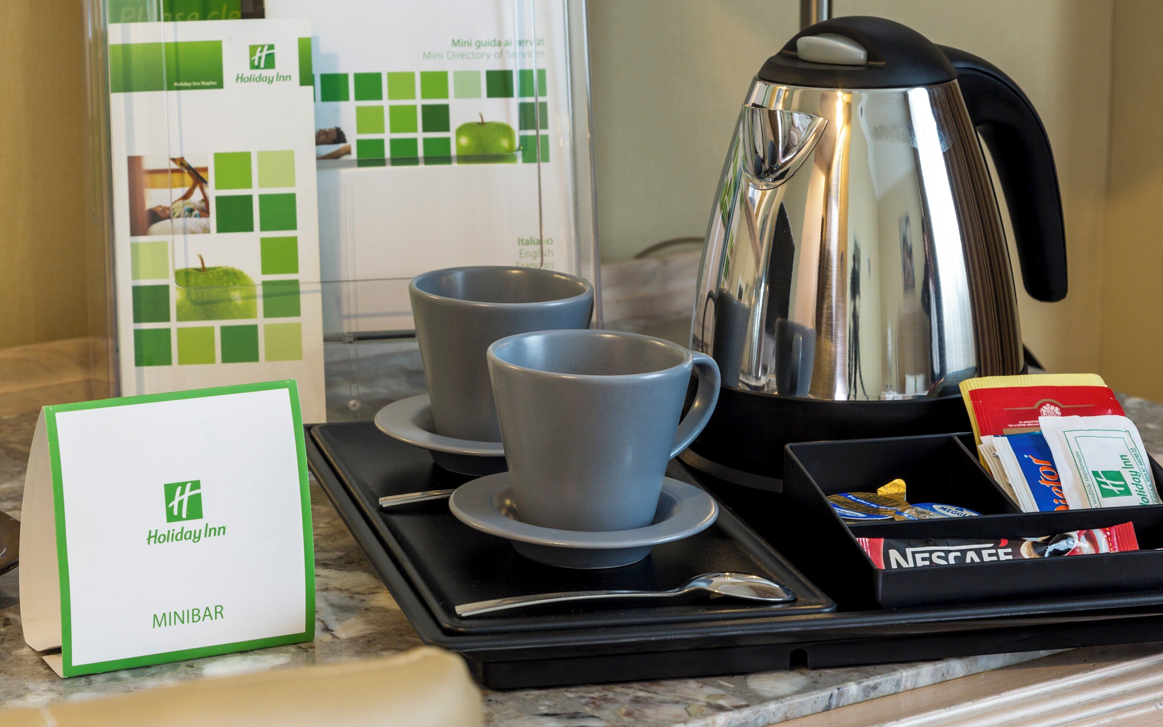 A breakfast setup with two cups, a coffee pot, a tray with a box of Nescafe, and a Holiday Inn sign.