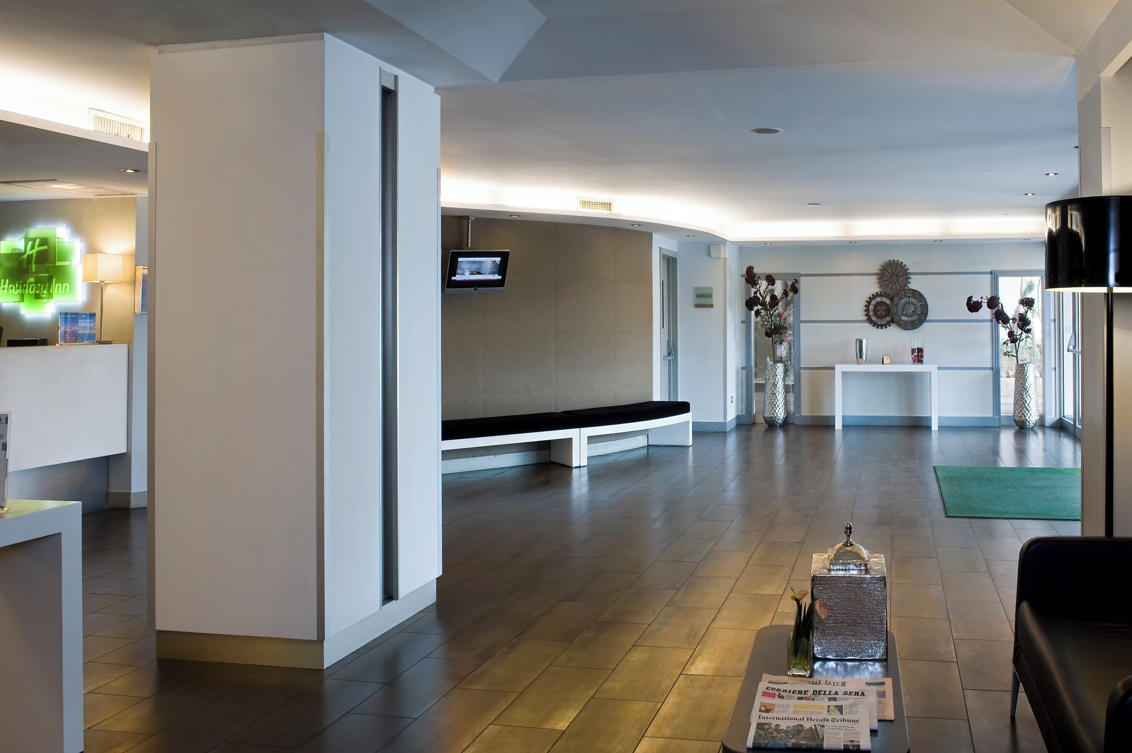 Un moderno vestíbulo de hotel con una recepción, una zona de estar y un televisor montado en la pared.