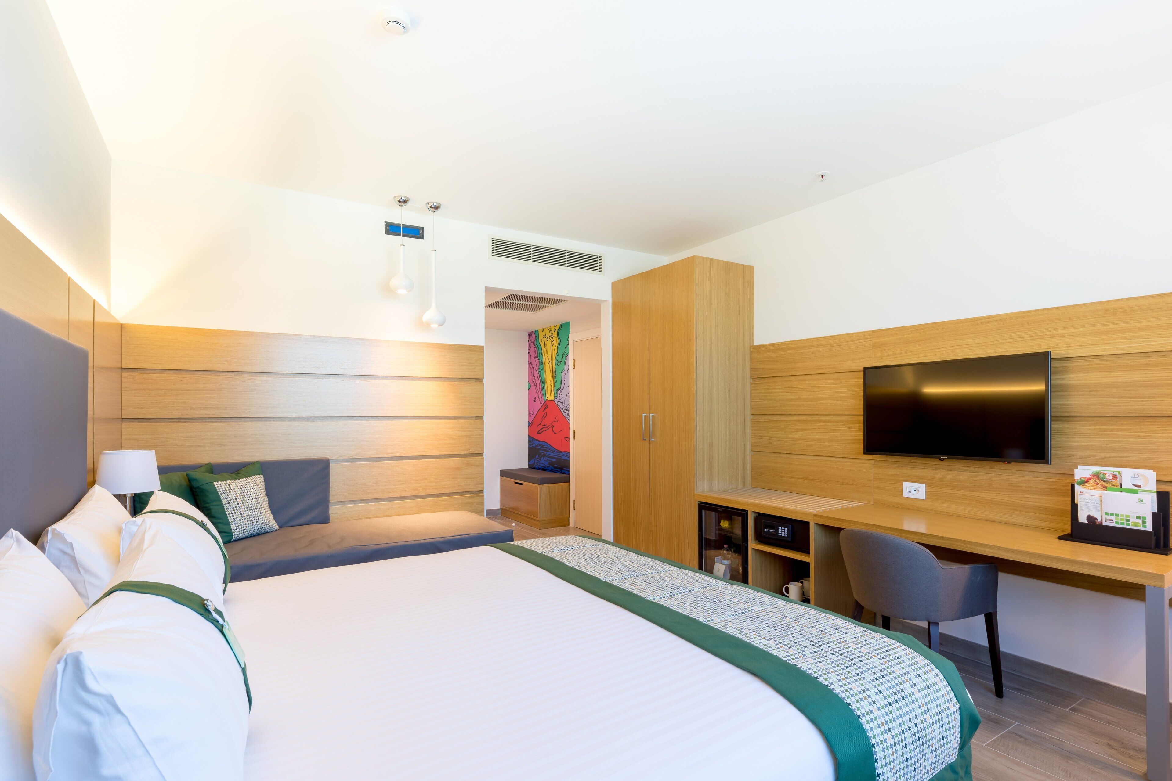 Une chambre d’hôtel avec un grand lit, un bureau, une télévision et une œuvre d’art colorée accrochée au mur.