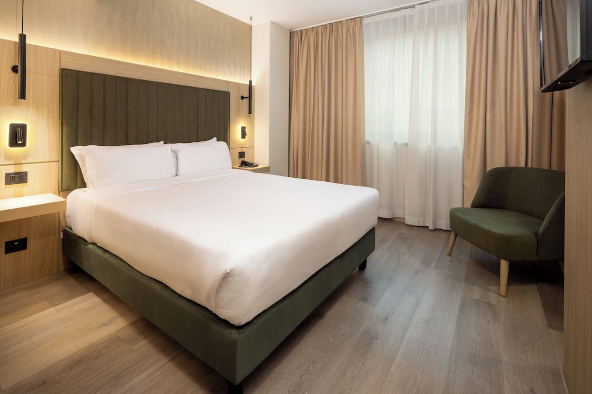 Une chambre d’hôtel avec un grand lit, des tables de chevet, une télévision et une chaise.