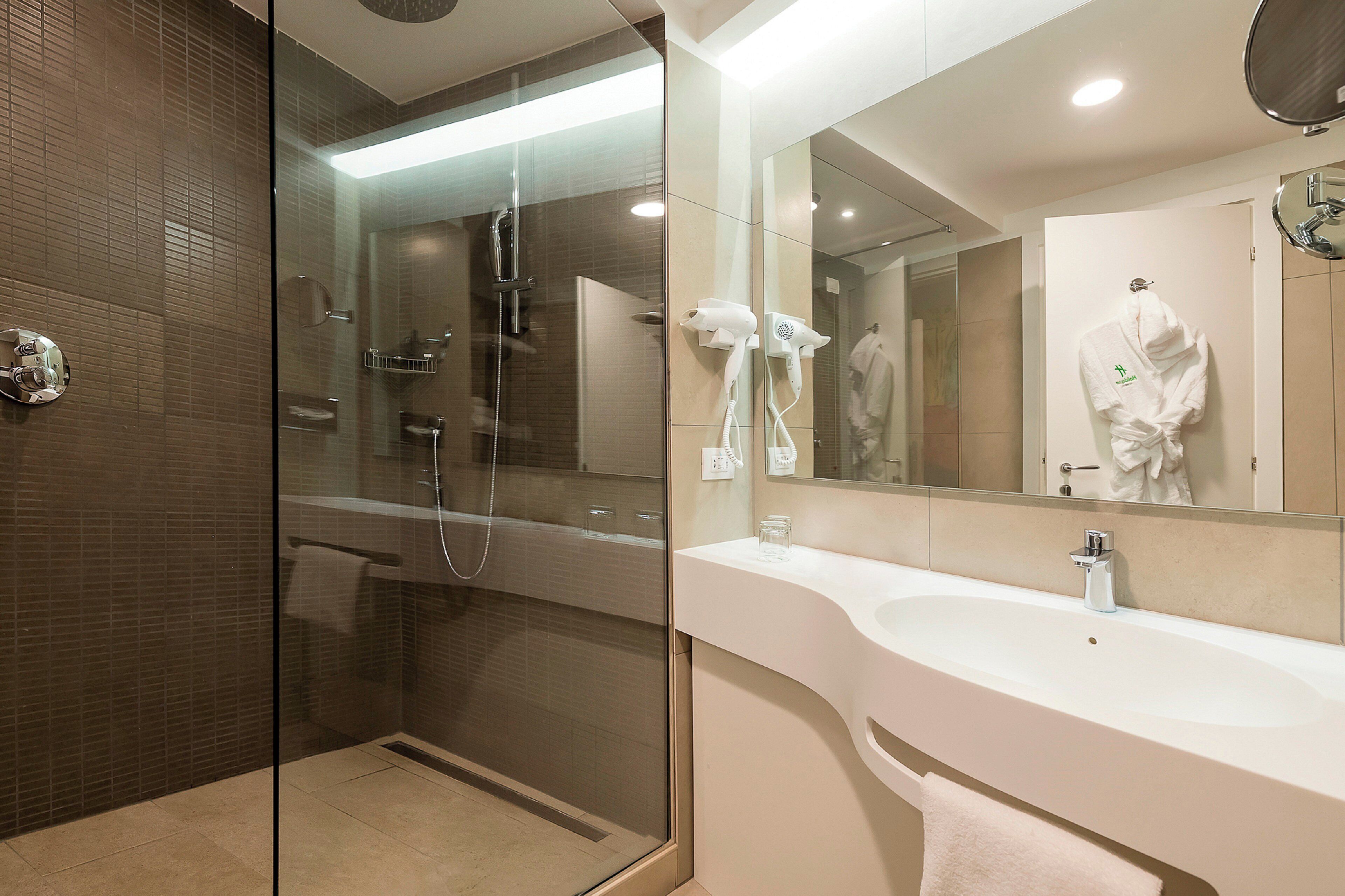 Un baño moderno con ducha de vidrio, lavamanos blanco y un espejo grande.