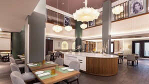 En modern hotellobby med en central ö, sittgrupper och ett högt tak med dekorativ belysning.