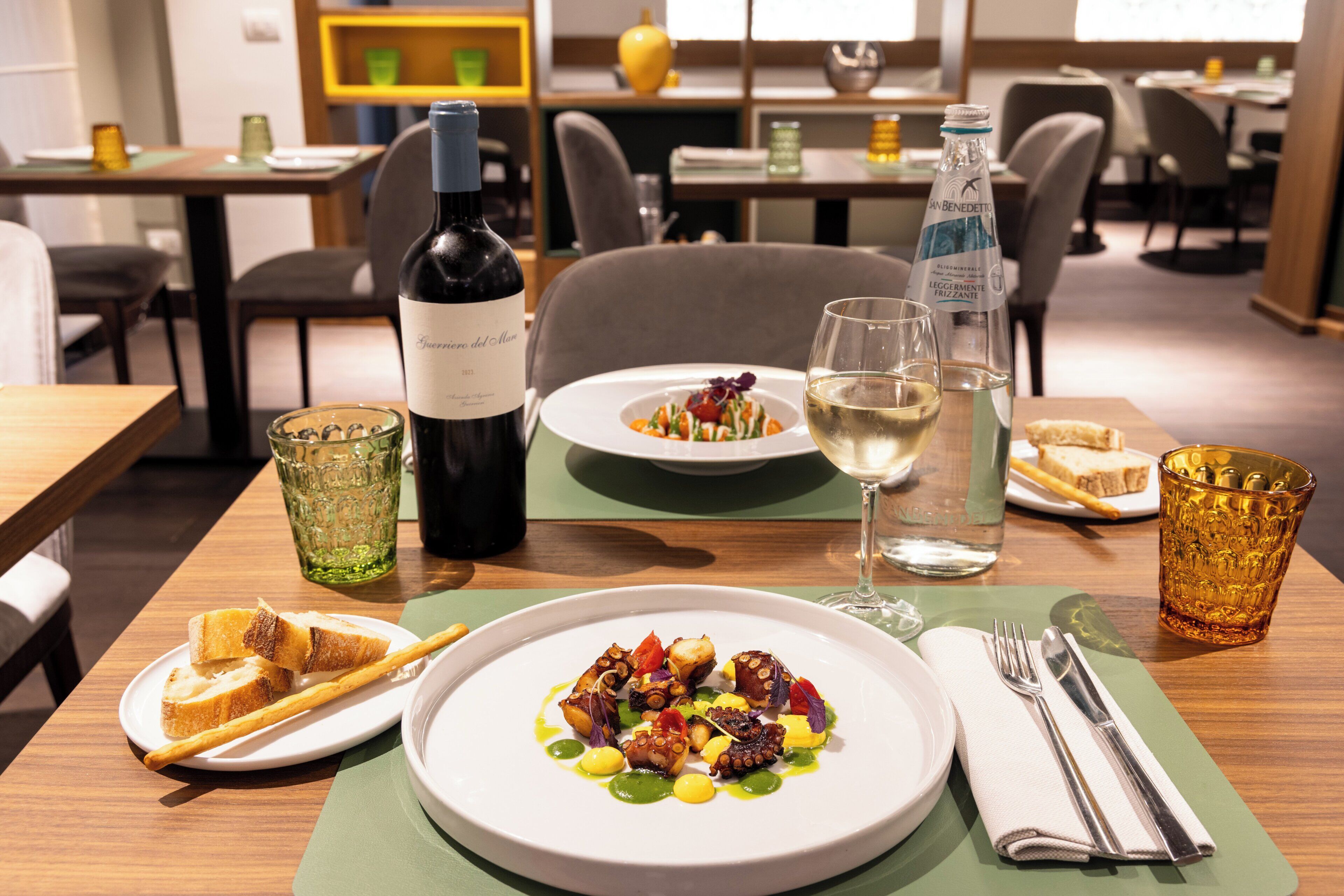 Une table à manger avec une assiette de nourriture, une bouteille de vin, un verre d’eau et un verre de vin.