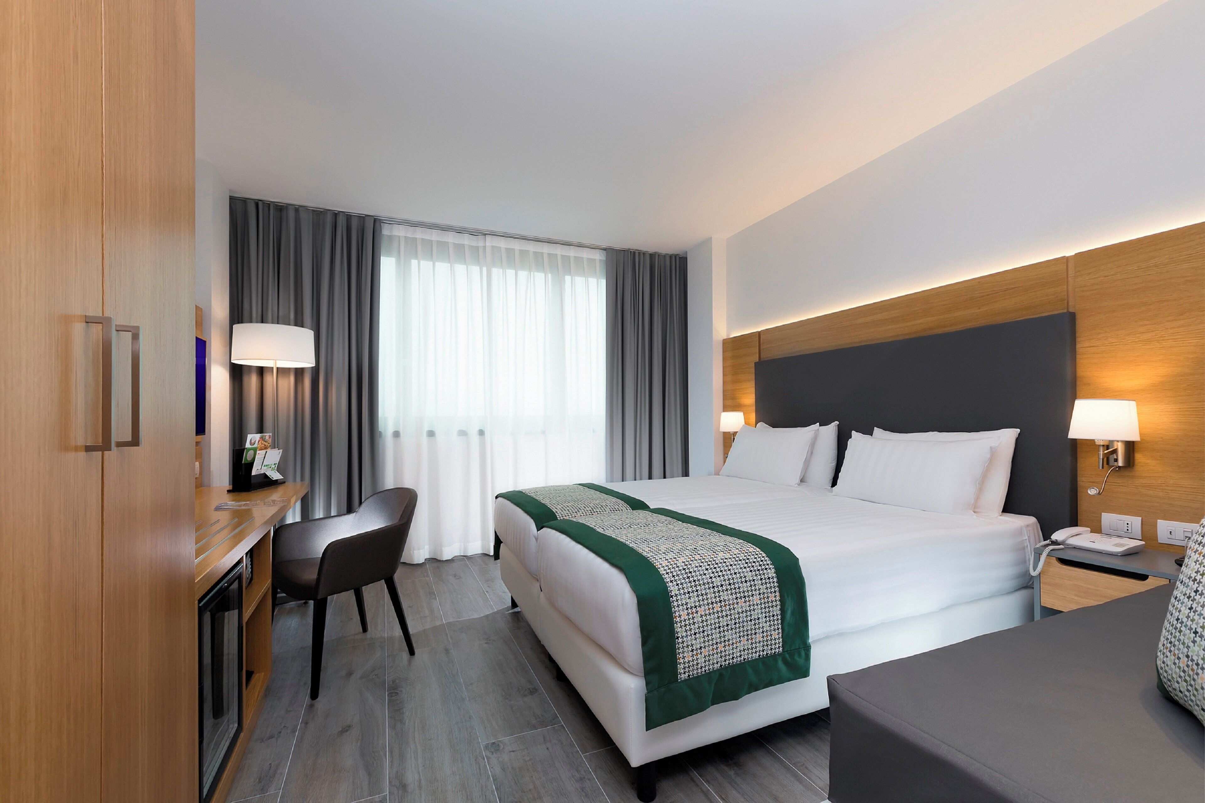 Una habitación de hotel con cama, escritorio, silla y mesita de noche con lámpara.