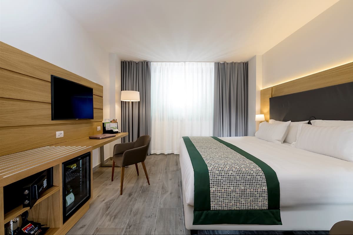 Une chambre d’hôtel comprenant un lit, un bureau avec une télévision, une chaise et un mini-bar.