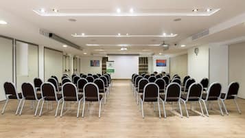 A conference room with rows of foldable chairs, a projector screen, and a clock on the wall.