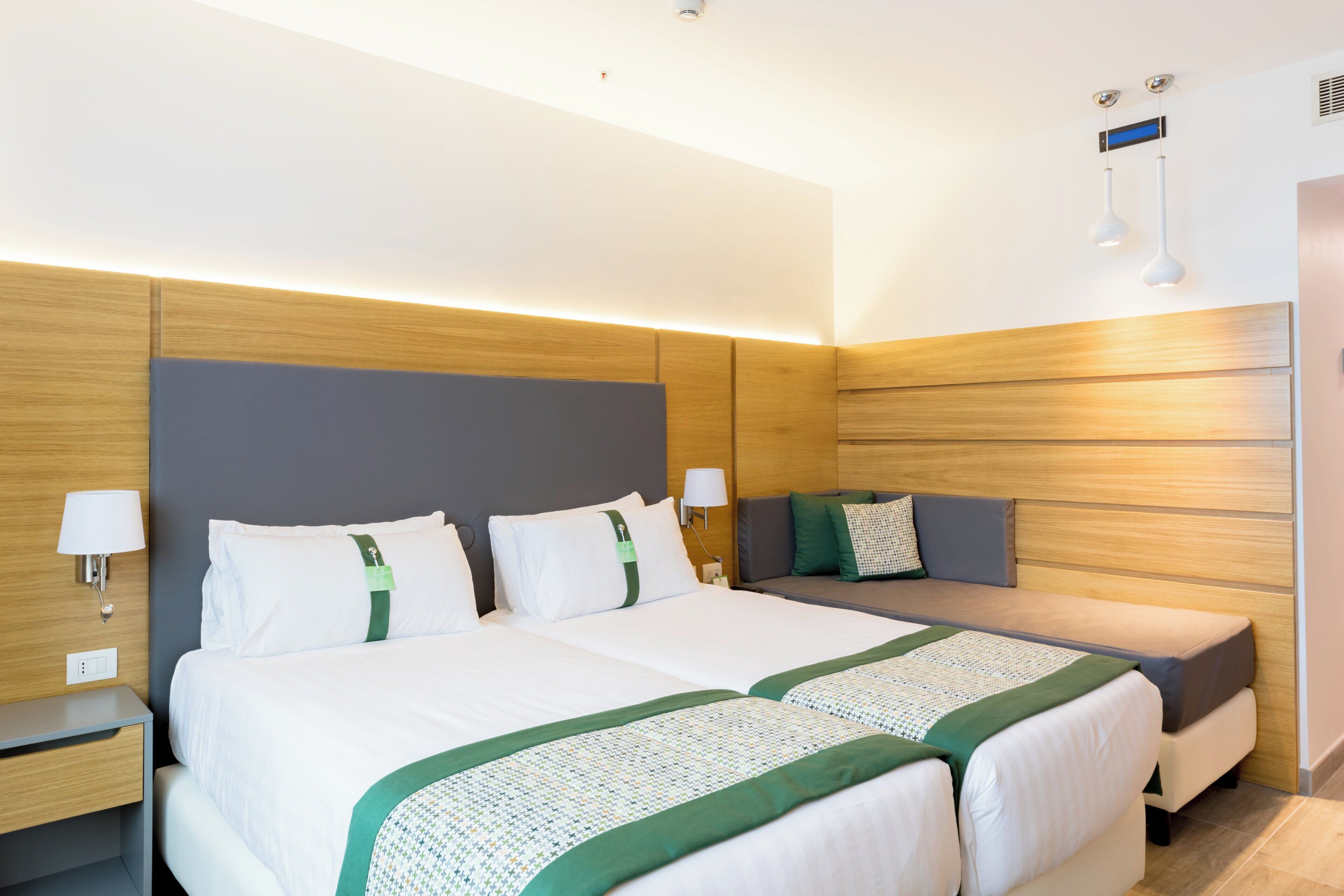 Habitación de hotel con cama doble, mesita de noche, sofá y lámpara de pared.