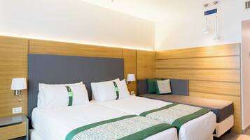 A hotel room with a double bed, a bedside table, a nightstand, a sofa, and a wall-mounted lamp.