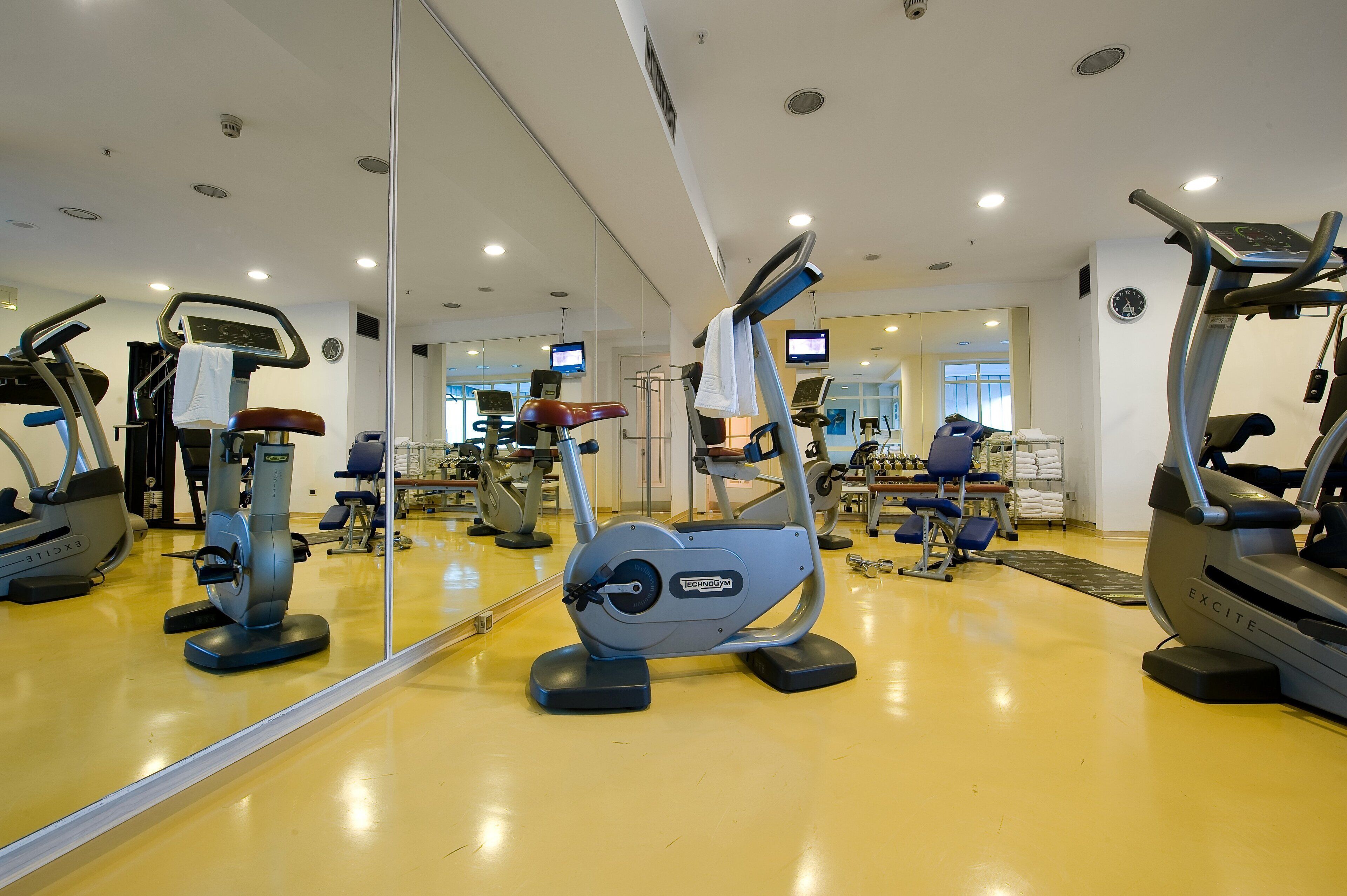 A gym with various exercise machines, a large mirror, and a clock on the wall.