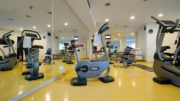 Un gimnasio con diversas máquinas de ejercicio, un espejo grande y un reloj en la pared.
