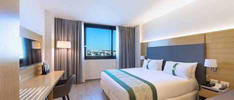 Quarto de hotel com cama, escrivaninha, cadeira e janela com cortinas.