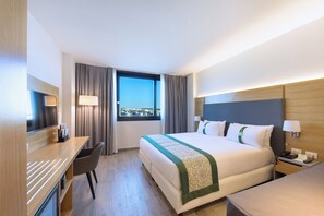 A hotel room with a bed, desk, chair, and a window with curtains.