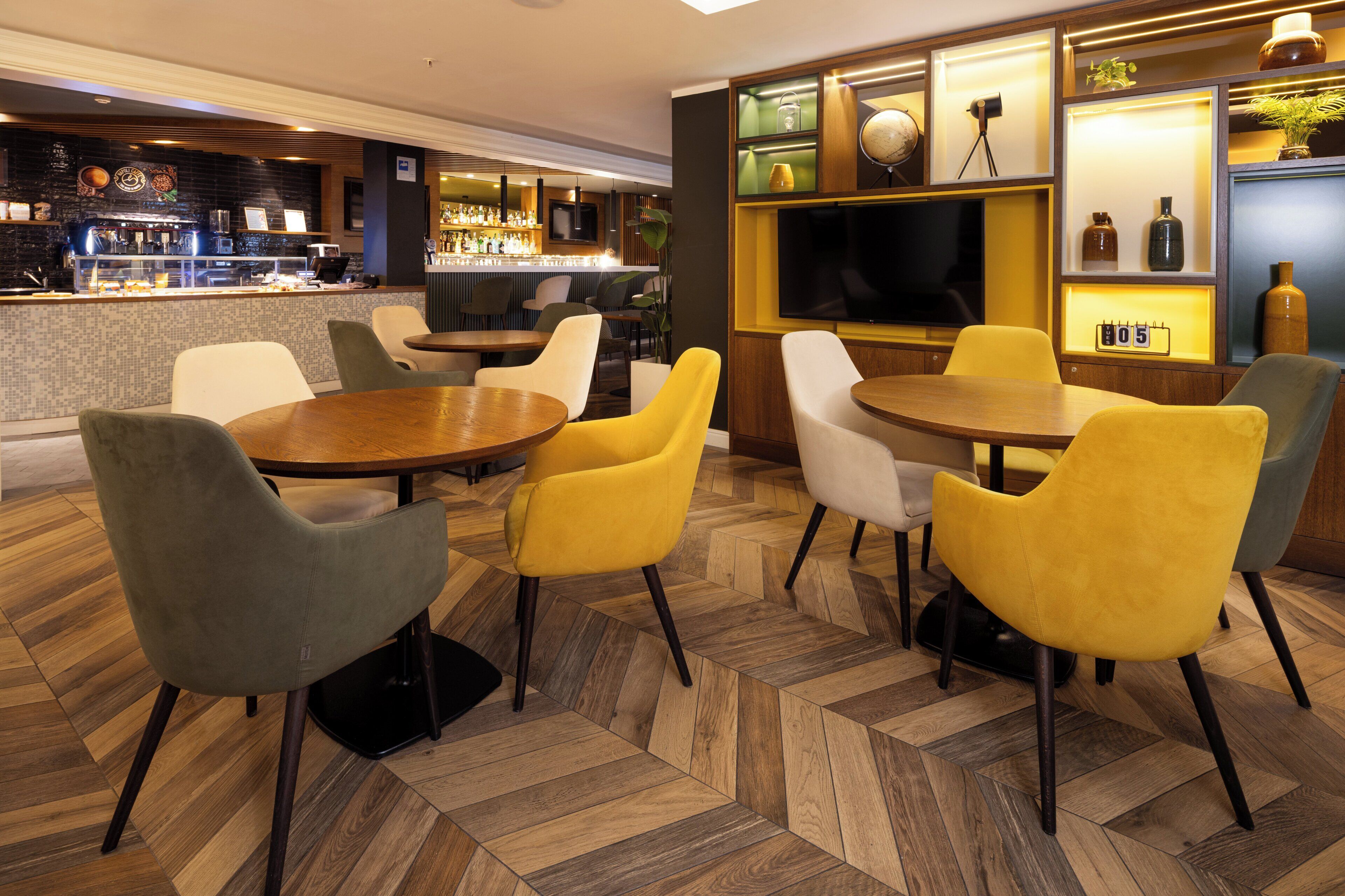 A restaurant with a bar area, multiple seating options including round tables and chairs, and a television screen.