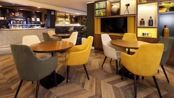 A restaurant with a bar area, multiple seating options including round tables and chairs, and a television screen.