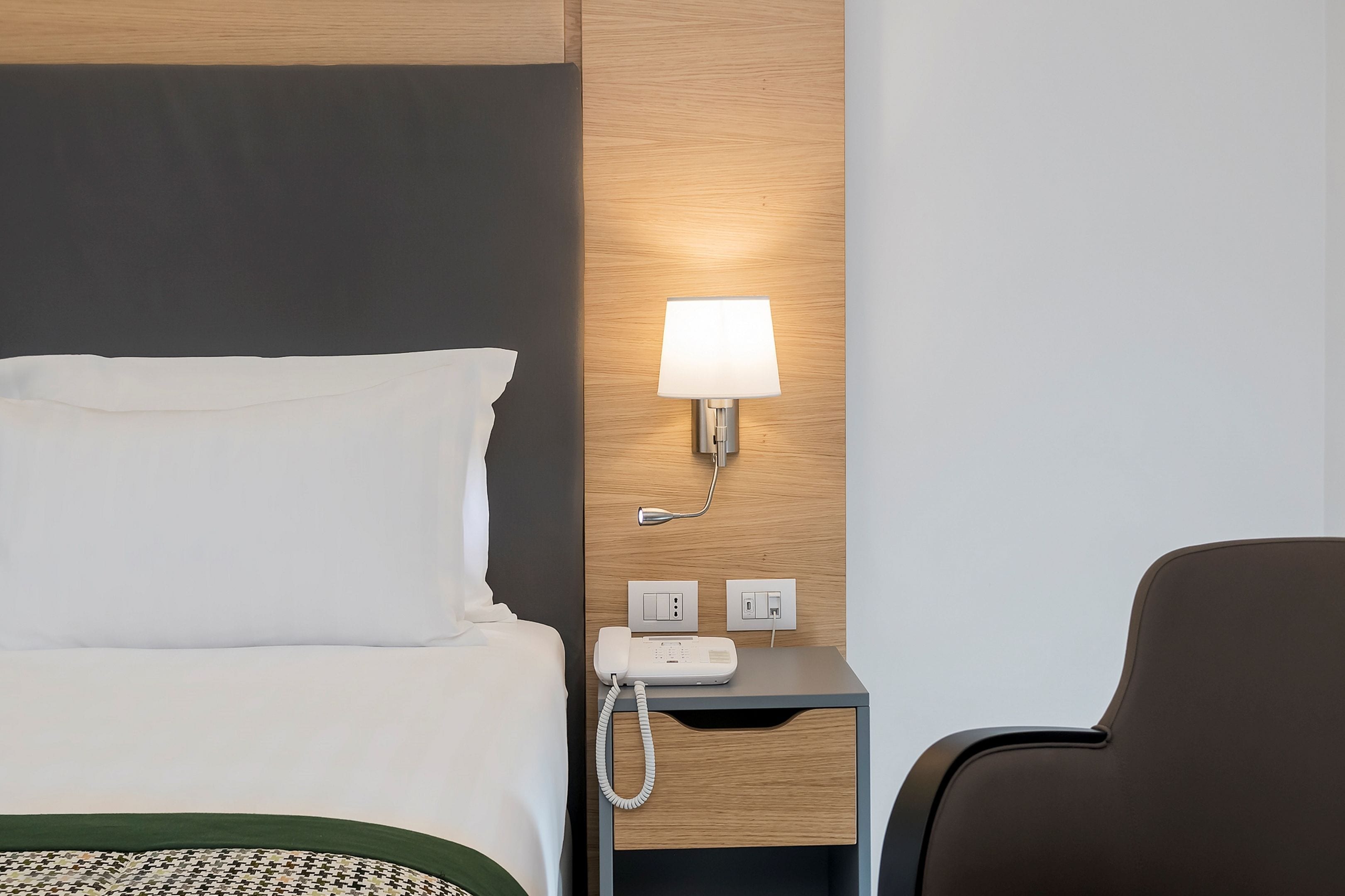 Ein Hotelzimmer mit Bett, Nachttischlampe, Telefon und Stuhl.