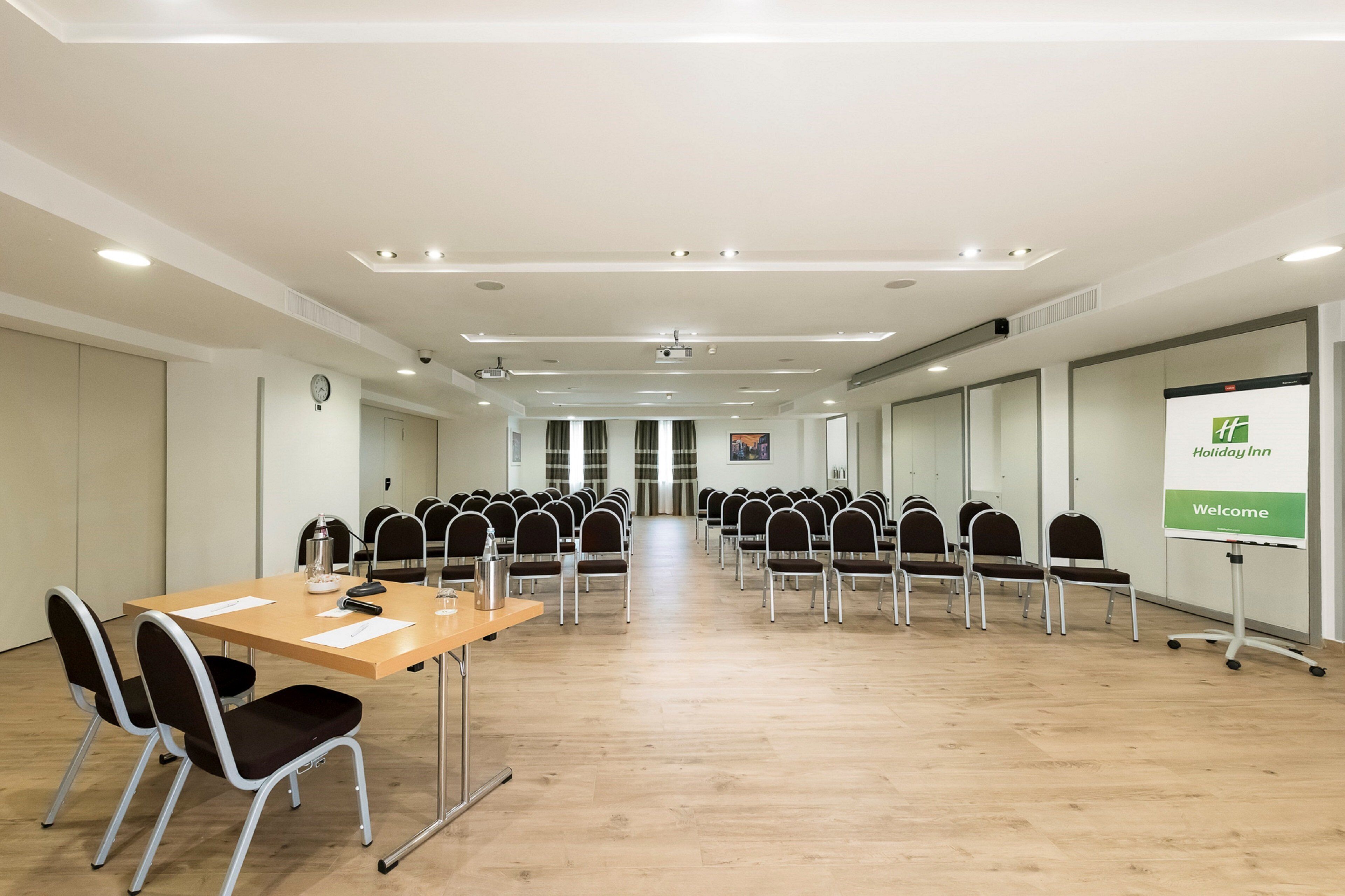 A conference room with a long table, chairs, a projector, and a presentation screen.