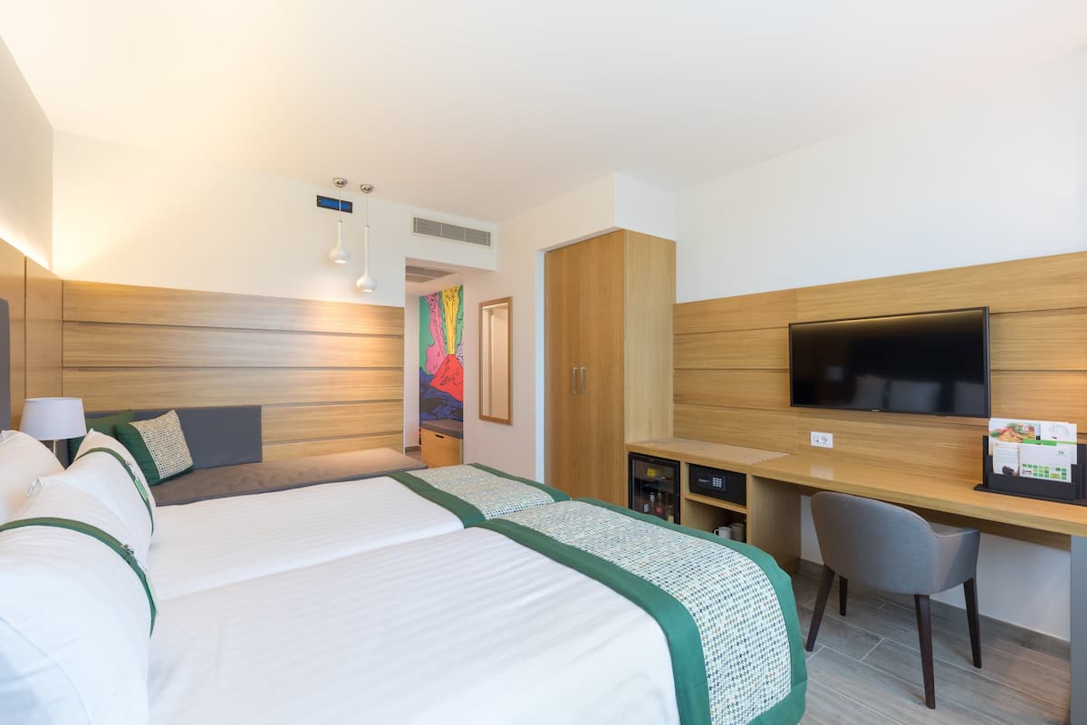 Une chambre d’hôtel avec un grand lit, un bureau avec une chaise, un téléviseur à écran plat et un petit réfrigérateur.