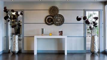 Un intérieur moderne avec une console blanche, des horloges décoratives et deux grands vases ornés de fleurs séchées.