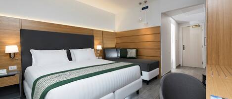 A modern hotel room with a large bed, a bedside table, a desk, and a chair.