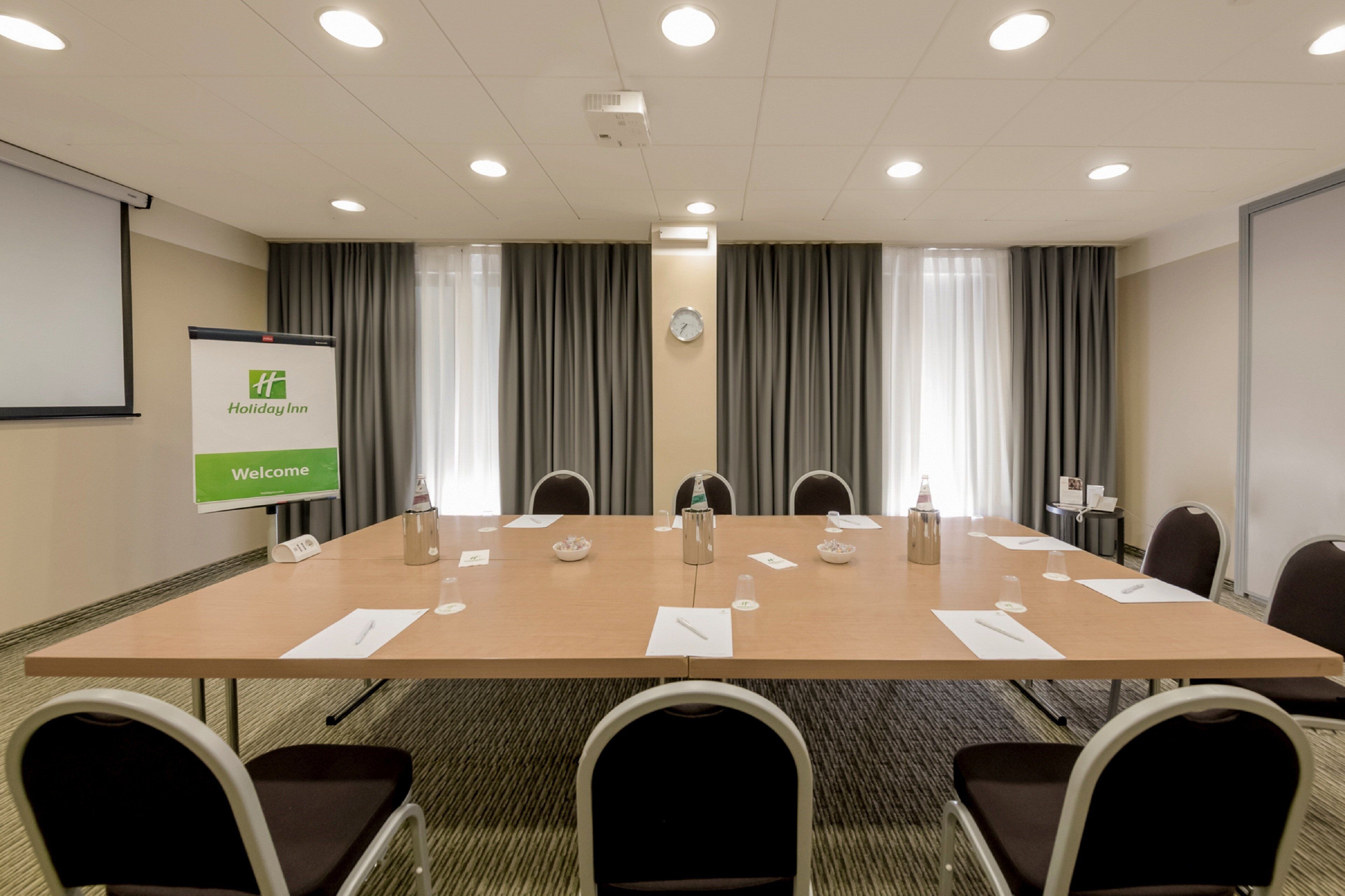 A conference room with a long table, chairs, a projector screen, and a clock on the wall.
