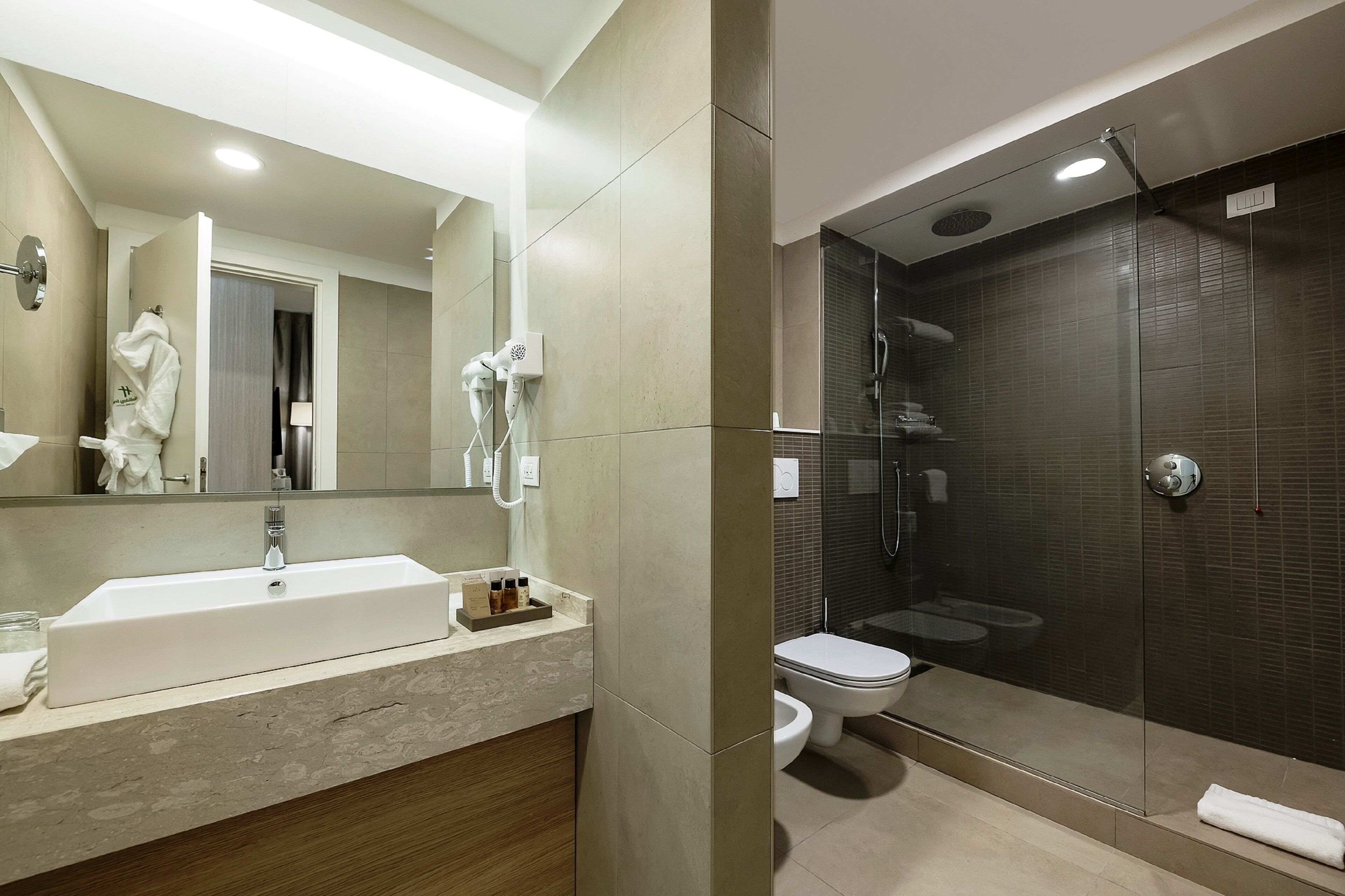 A modern bathroom with a large sink, mirror, and glass-enclosed shower.