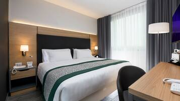 Una habitación de hotel con una cama grande, lámparas de noche, un escritorio con teléfono y una ventana con cortinas.