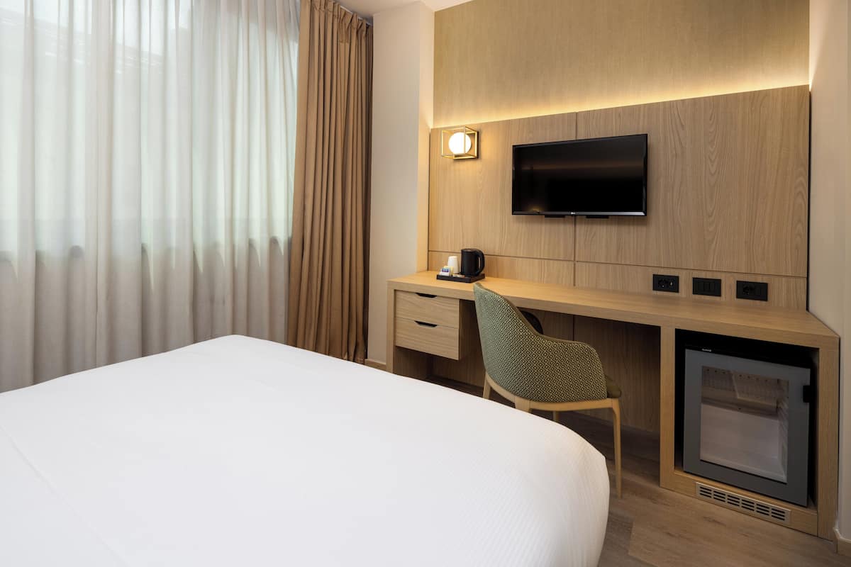 Une chambre d’hôtel comprenant un lit, un bureau avec une chaise, une télévision et un minibar.