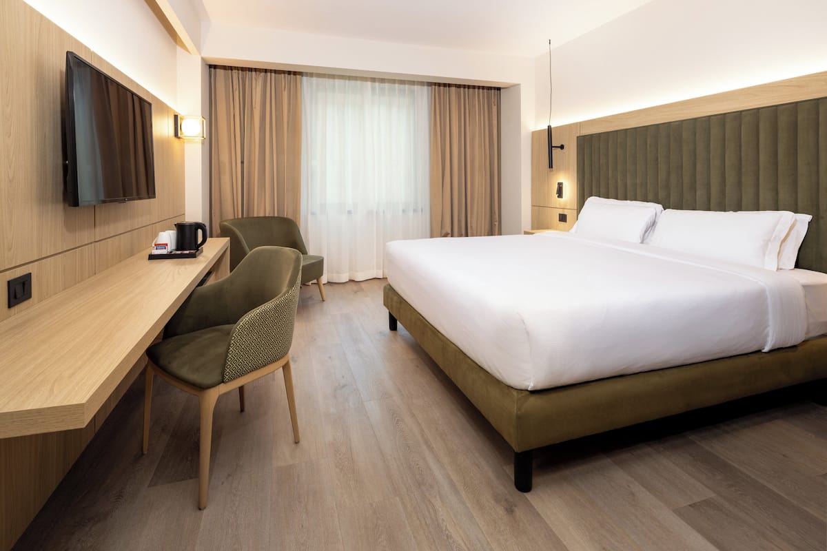Une chambre d’hôtel comprenant un lit, un bureau avec une chaise, une télévision et une fenêtre avec des rideaux.