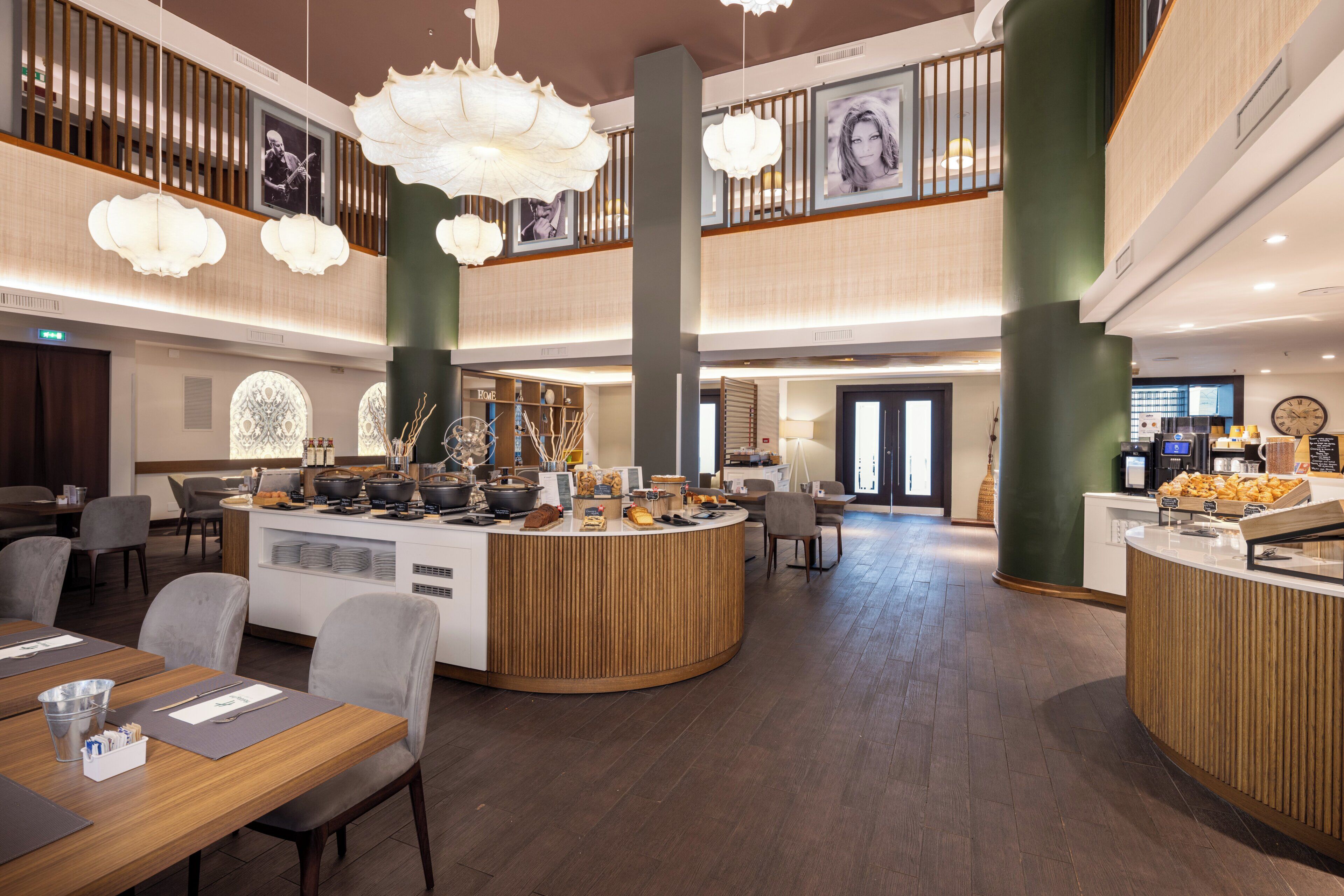 A spacious hotel lobby with a central reception desk, seating areas, and a high ceiling with hanging light fixtures.
