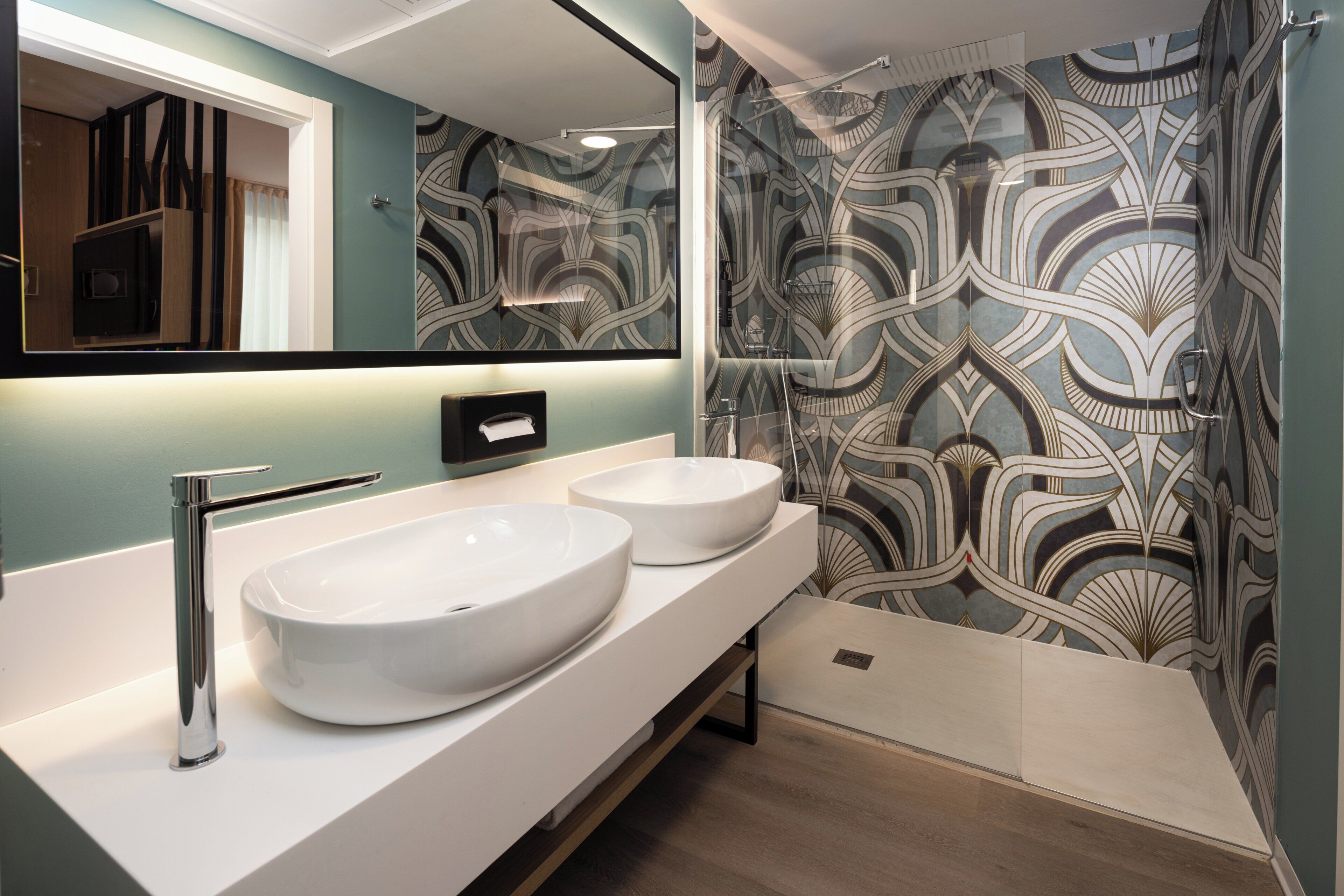 A bathroom with two large white sinks, a chrome faucet, a mirror, and a shower with a patterned wall.