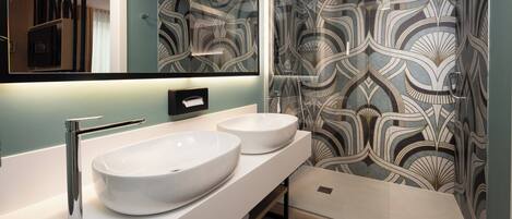 Un bagno con due ampi lavandini bianchi, un rubinetto cromato, uno specchio e una doccia con rivestimenti decorati.