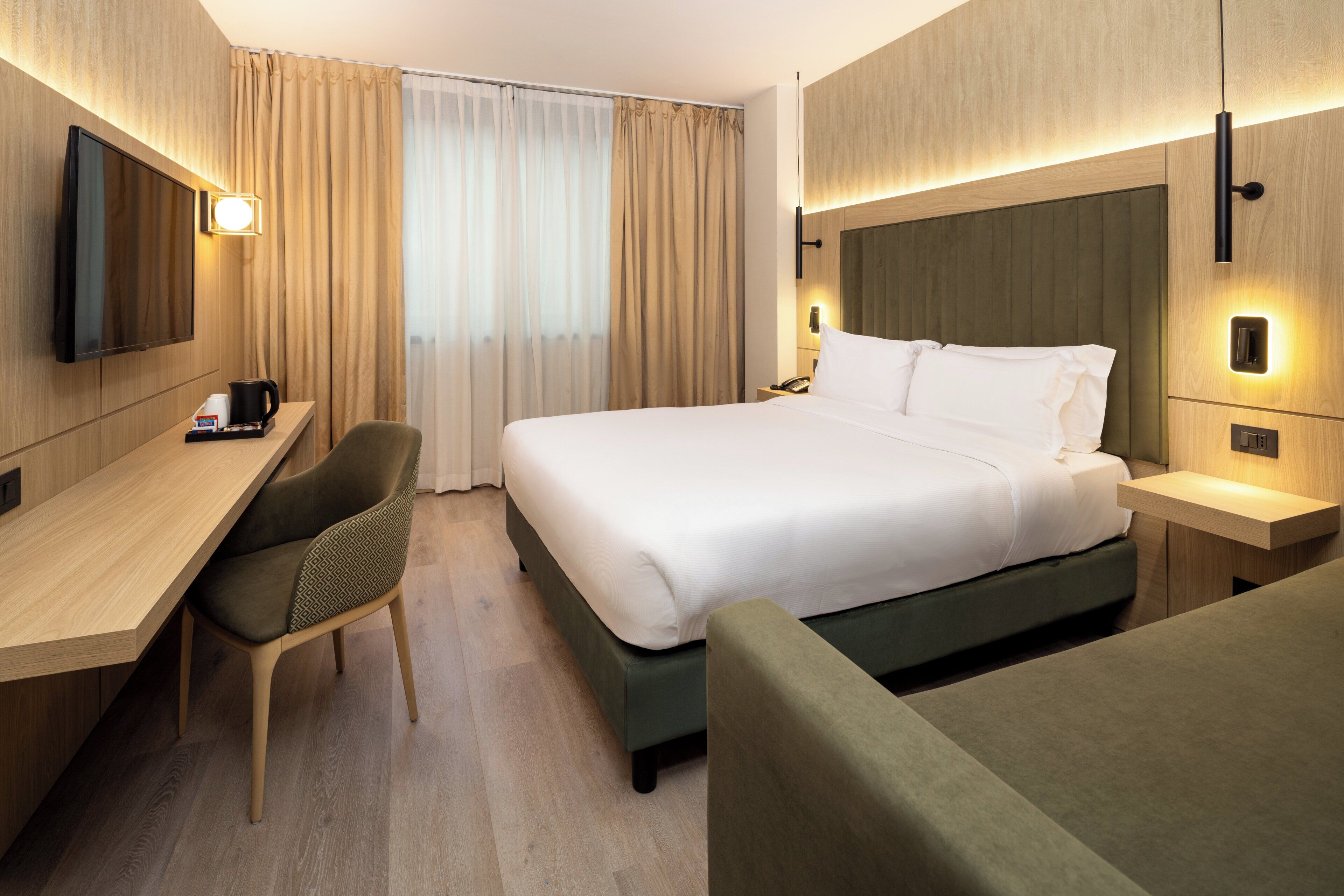 Habitación de hotel con cama, escritorio, silla, televisor y mesita de noche.