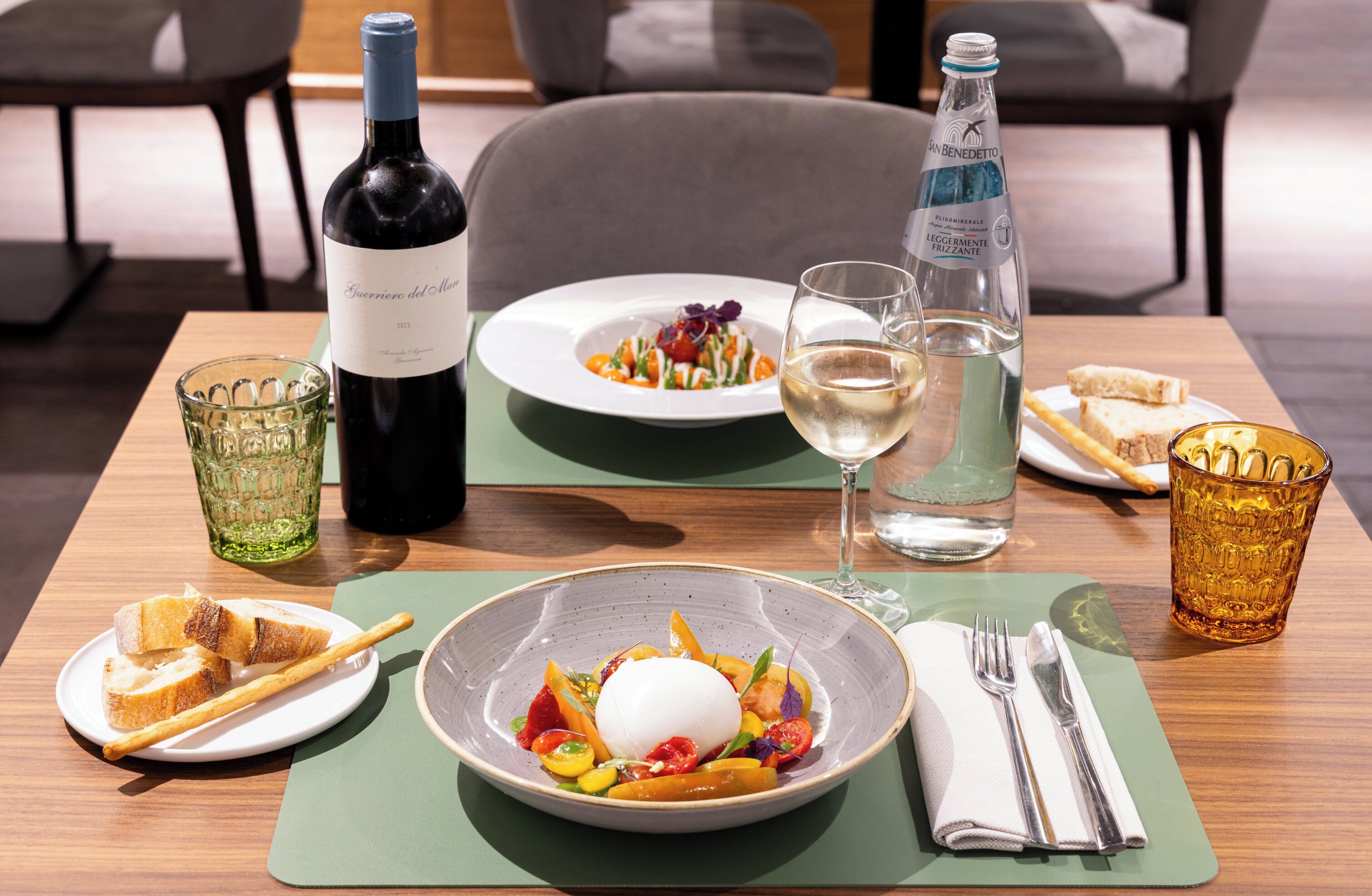 A dining table with plates of food, a bottle of wine, glasses, and cutlery.