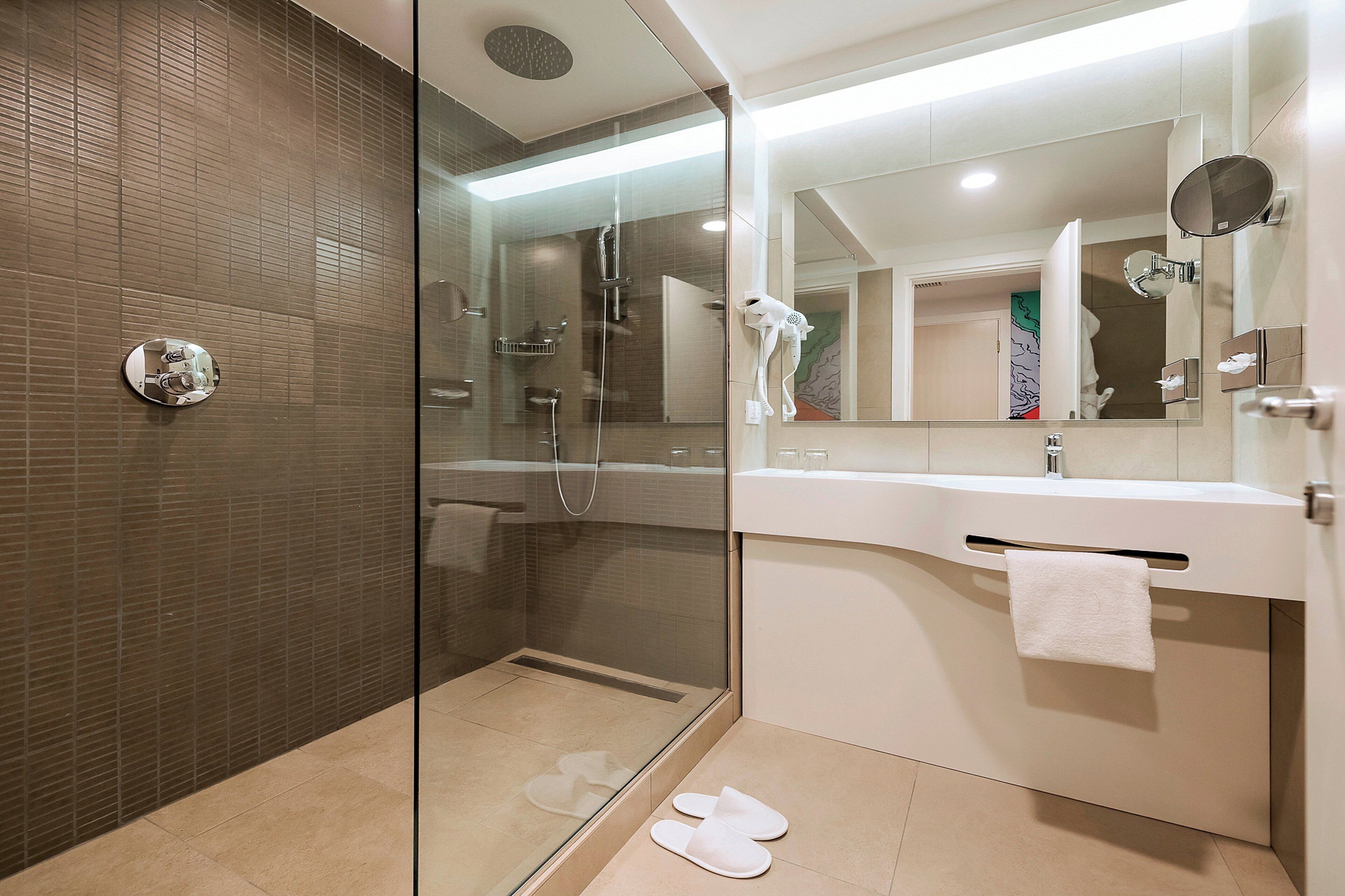 Un baño moderno con ducha de vidrio, lavamanos blanco y espejo grande.