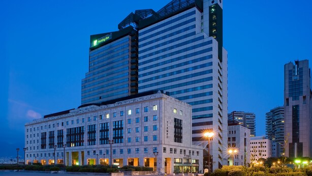 Ett hotell med modern design, som kännetecknas av en stor, väl synlig "Honda"-skylt på den högsta byggnaden. Hotellet har flera våningar med stora fönster och en väl upplyst fasad.