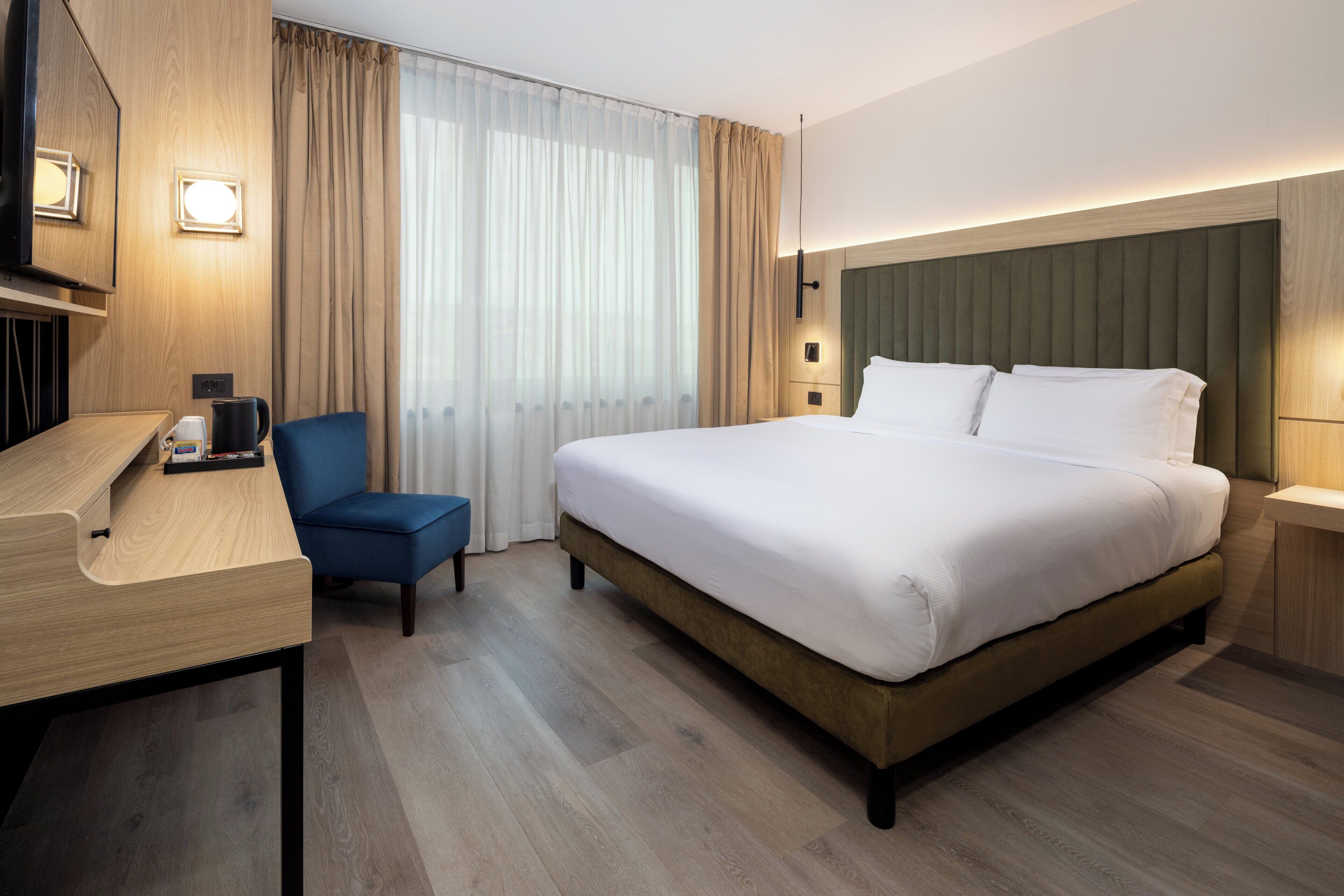 A hotel room with a large bed, a desk, a chair, and a television.