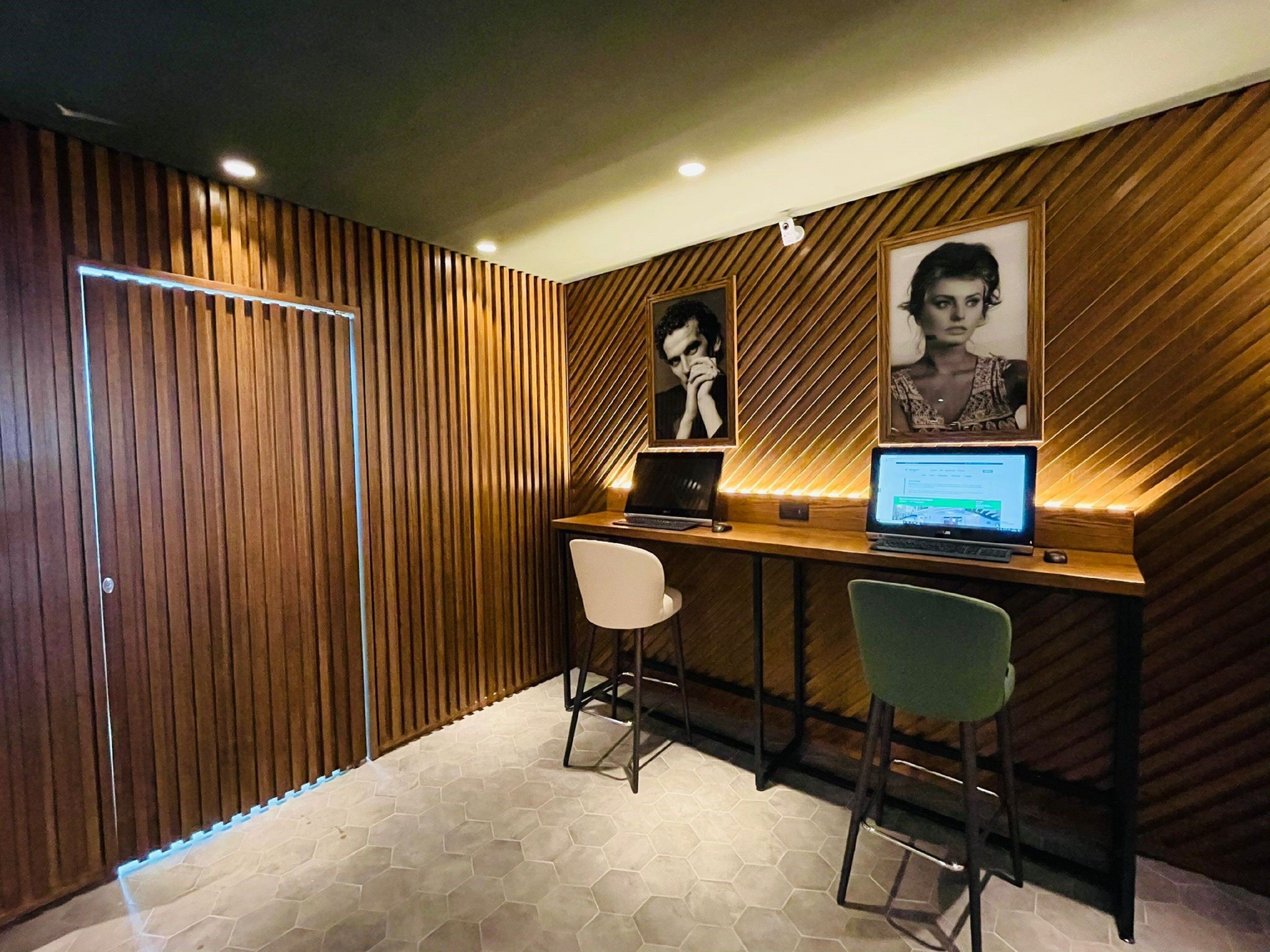 Una habitación moderna con pared de listones de madera, dos taburetes tipo bar, un escritorio con una computadora portátil y cuadros en la pared.