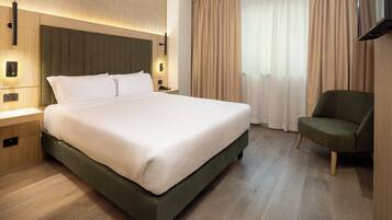 Una habitación de hotel con una cama grande, mesitas de noche, televisor y una silla.