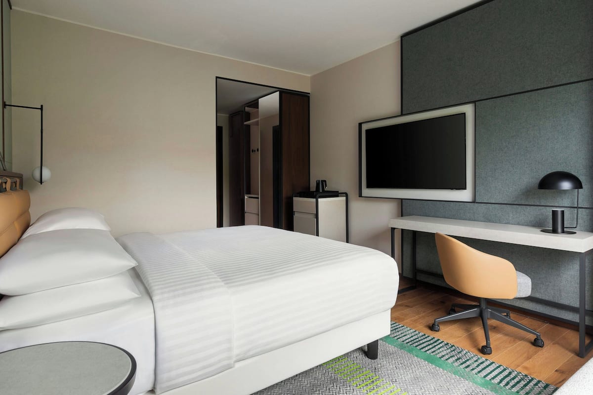 Quarto de hotel moderno com cama, escrivaninha, cadeira, televisão e guarda-roupa.