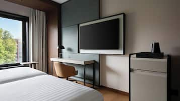 A hotel room with a large bed, a desk, a chair, a TV, and a minibar.